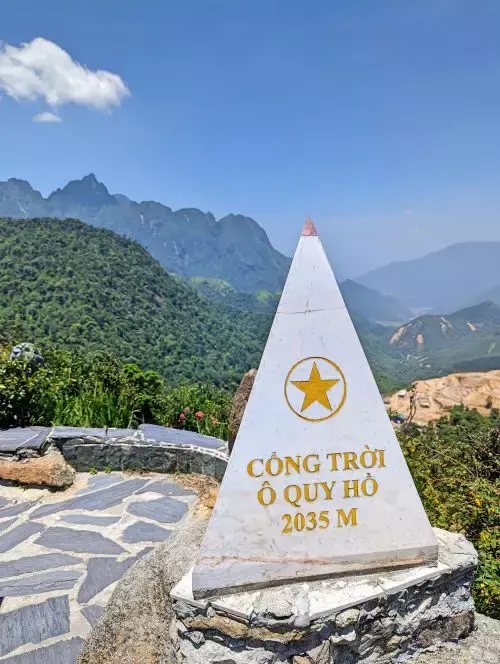 A bronze color triangular landmark on top of a turtle sculpture with the Sapa Gate of Heaven in the background