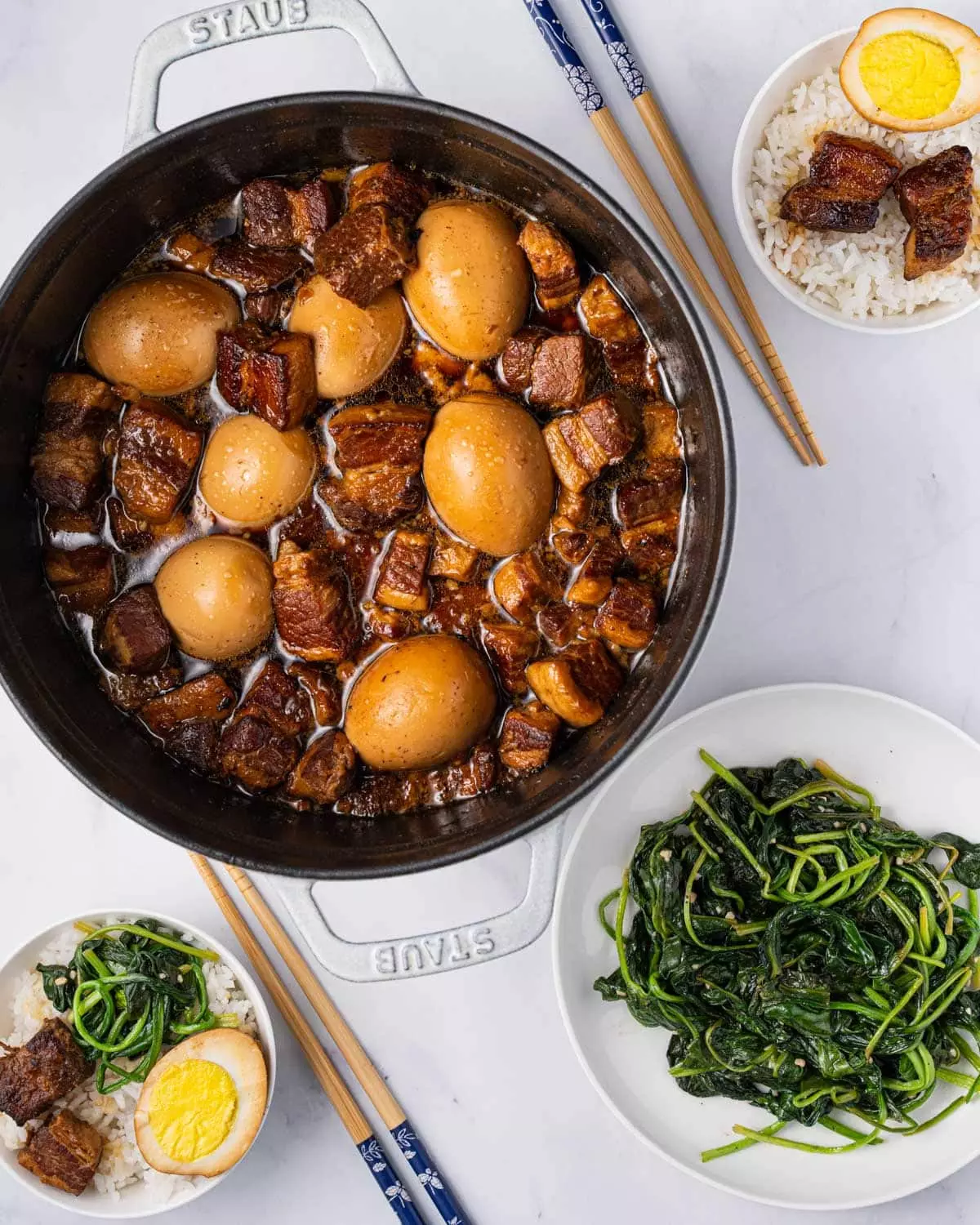 pot of thit kho with two bowls of rice and a side plate of green vegetables.